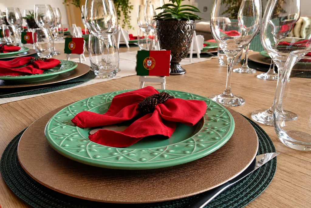 Mesa posta para jantar português em casa com pratos verdes, guardanapos vermelhos e bandeiras de Portugal