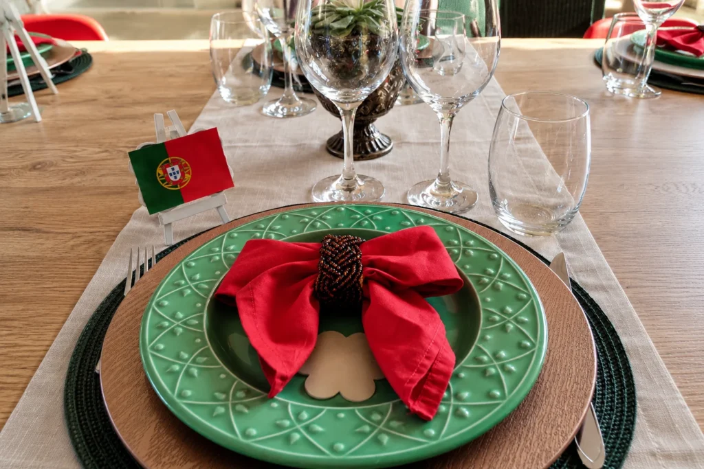 Lugar à mesa para jantar português em casa com prato verde, guardanapo vermelho e bandeira de Portugal